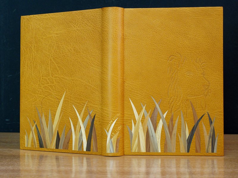  Joseph Kessel - Le lion - Reliure plein oasis à charnières. Décor en marqueterie de paille de seigle. La silhouette du lion est estampée. Gardes en daim avec un liseré de paille. Dorure à l'or de Stéphane Gangloff.